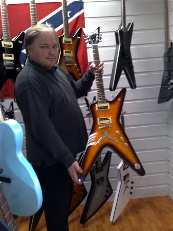 Alf Arne Hammer viser en Dean-gitar foran veggen i butikken